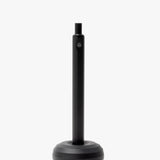 A sleek desk accessory, the HMM Paperweight Pen Stand (Black) features a round, weighted aluminum base and a vertical slot for upright pen storage. Plain white background. Text at bottom: Pen sold separately.