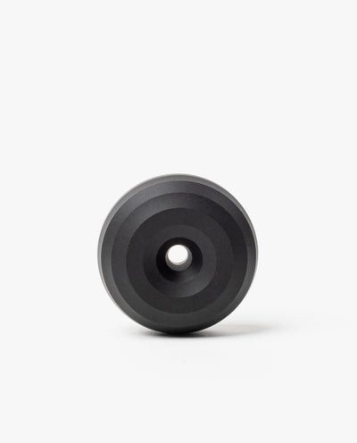 The HMM Paperweight Pen Stand (Black) is a circular aluminum piece with concentric raised rings and a central hole, shown on a plain white background.