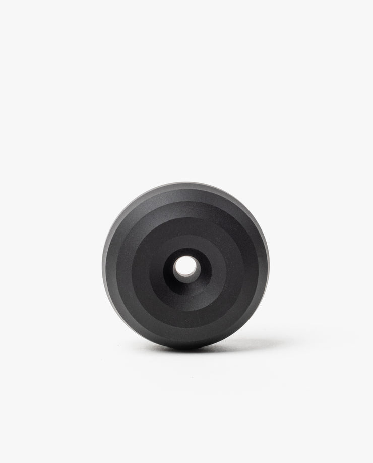 The HMM Paperweight Pen Stand (Black) is a circular aluminum piece with concentric raised rings and a central hole, shown on a plain white background.