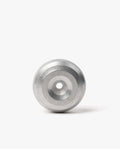 A modern desk accessory, the HMM Paperweight Pen Stand (Raw) features a metallic, circular design with concentric rings and a central hole. Crafted from sleek aluminum, it stands upright on a white background, serving as both an elegant paperweight and a stylish pen stand.