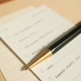 The Ugmonk Pen (Leuchtturm1917 Drehgriffel - Black) rests on a to-do list with handwritten tasks and empty checkboxes on lined paper atop a light wooden surface.