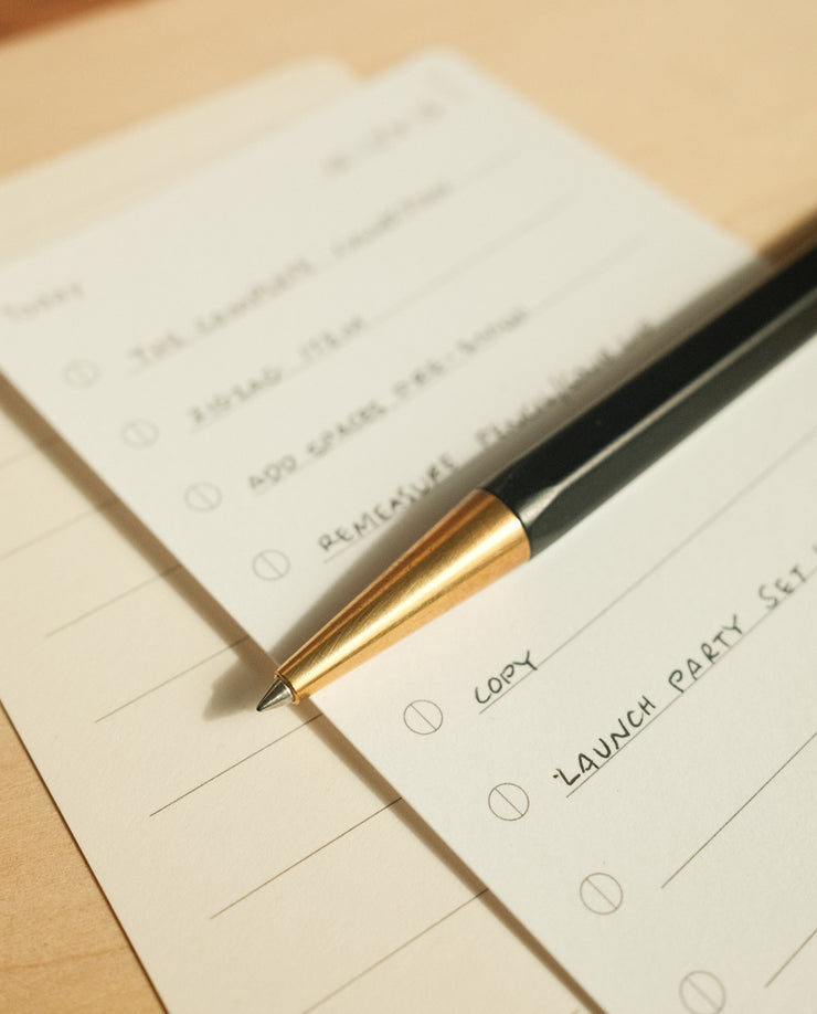 A close-up of The Analog Bundle (Walnut) resting on a to-do list with handwritten tasks like “LAUNCH PARTY SETUP” and “REMEMBER PRESENT,” all placed on a light wooden surface.