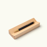 The Ugmonk Pen (Leuchtturm1917 Drehgriffel - Black) sits on a light wooden pen tray against a plain white background. Text below says, “Wood Pen Tray sold separately.”.