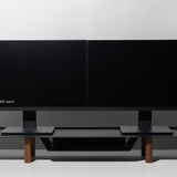 Two black 24-inch computer monitors are side by side on a Gather Large Monitor Stand (Black/Walnut) with wooden legs, set against a white background. The left monitor displays the text: “Monitors shown: 24” each.”.