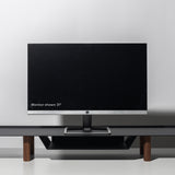 A 21-inch computer monitor sits on the Gather Large Monitor Stand (Black/Walnut) against a plain light gray background. The screen is off, drawing attention to the stand’s sleek, minimalist design and space-saving functionality.