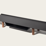 The Gather Large Monitor Stand (Black/Walnut) features a modern rectangular black top, four walnut cylindrical legs, and a black shelf beneath—perfect as a space-saving monitor stand. Shown against an off-white background.