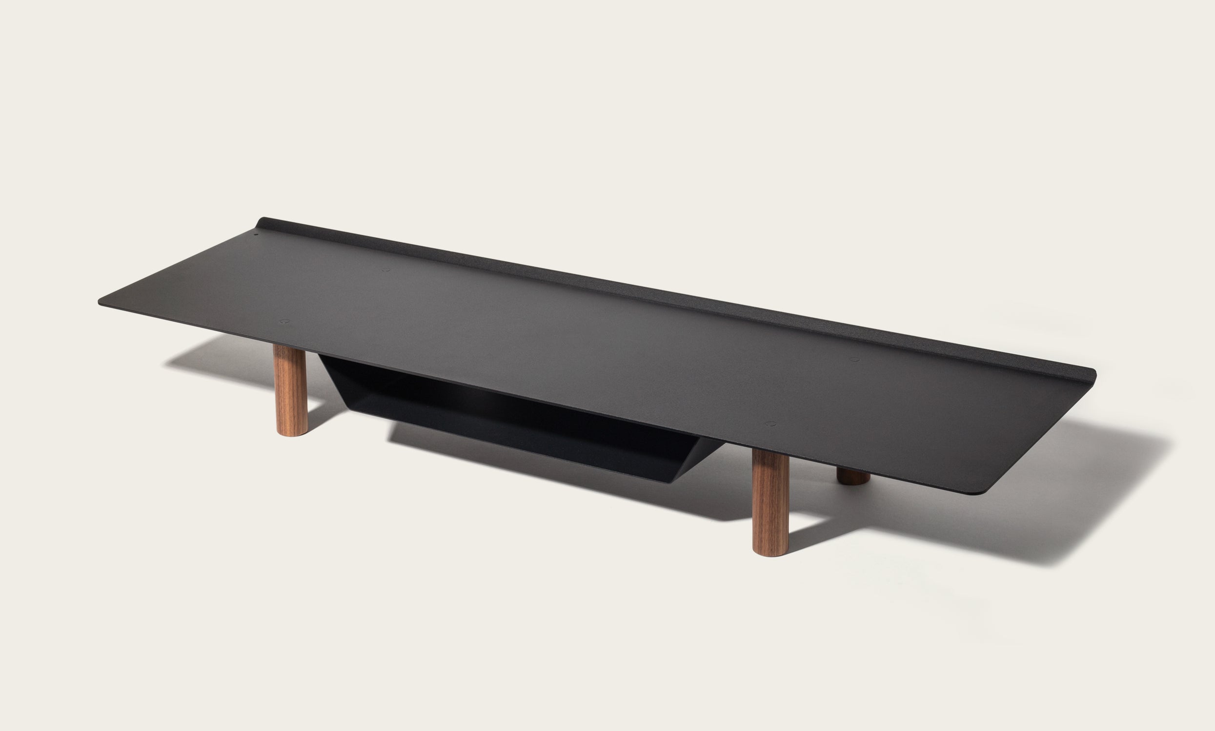 The Gather Large Monitor Stand (Black/Walnut) features a modern rectangular black top, four walnut cylindrical legs, and a black shelf beneath—perfect as a space-saving monitor stand. Shown against an off-white background.
