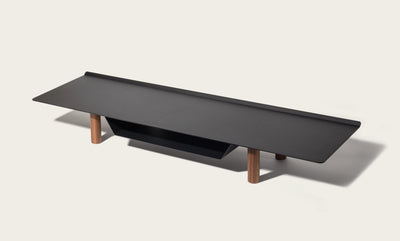 The Gather Large Monitor Stand (Black/Walnut) features a modern rectangular black top, four walnut cylindrical legs, and a black shelf beneath—perfect as a space-saving monitor stand. Shown against an off-white background.