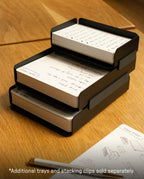 A black steel Capture Bundle (Small Tray + Large Tray) holds index cards with handwritten notes on a wooden desk. More Capture Cards and a pen are nearby. Text at the bottom: Additional trays and stacking clips sold separately.