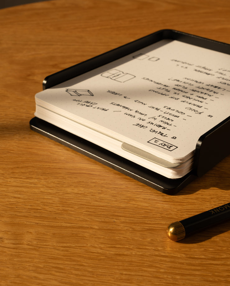 The Analog Capture Kit - 2 Large (Black Aluminum) sits on a wooden table, holding a stack of dot grid cards filled with handwritten black ink notes and drawings. A black pen rests nearby.