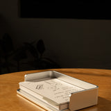 A silver aluminum Analog Capture Kit - Small sits on a wooden table, holding dot grid cards. Sunlight creates warm shadows while a few extra cards from the kit are scattered close by. The background is dark and blurred.