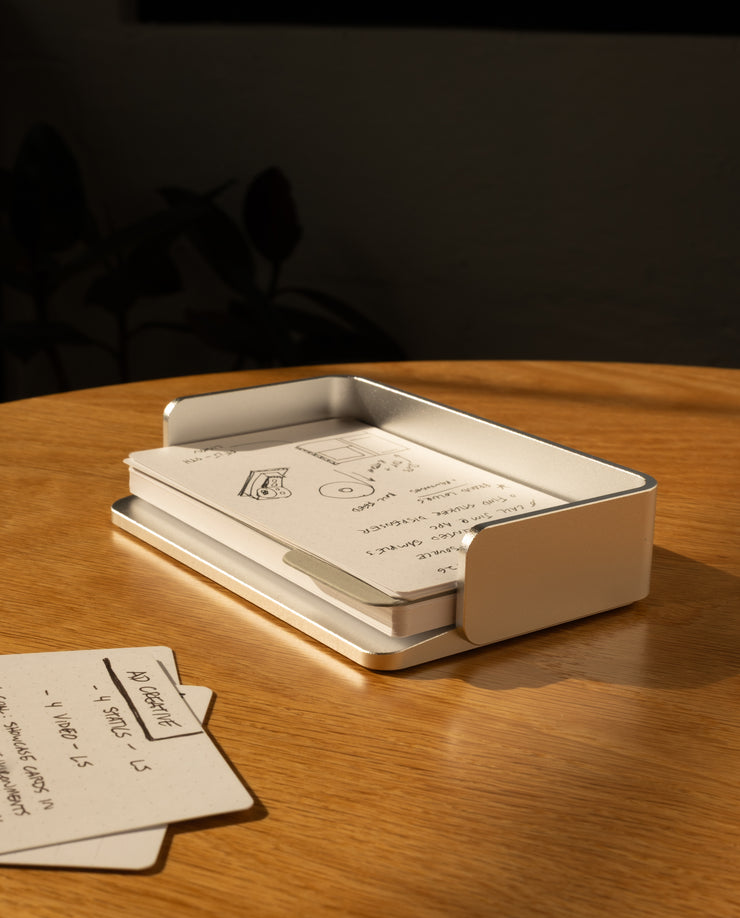 A silver aluminum Analog Capture Kit - Small sits on a wooden table, holding dot grid cards. Sunlight creates warm shadows while a few extra cards from the kit are scattered close by. The background is dark and blurred.