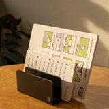 The Complete Analog Collection (Black Aluminum) holds two open notebooks on a wooden desk, one featuring colorful diagrams and the other with handwritten notes. Sunlight from a window casts warm shadows across the organized workspace.