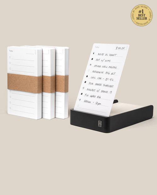 Three stacks of white task cards are shown beside a black aluminum card holder featuring a handwritten to-do list. A gold #1 Best Seller badge highlights the Analog Daily Focus Kit + 3 Refills (Black Aluminum) productivity system.