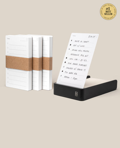 Three stacks of white task cards are shown beside a black aluminum card holder featuring a handwritten to-do list. A gold #1 Best Seller badge highlights the Analog Daily Focus Kit + 3 Refills (Black Aluminum) productivity system.