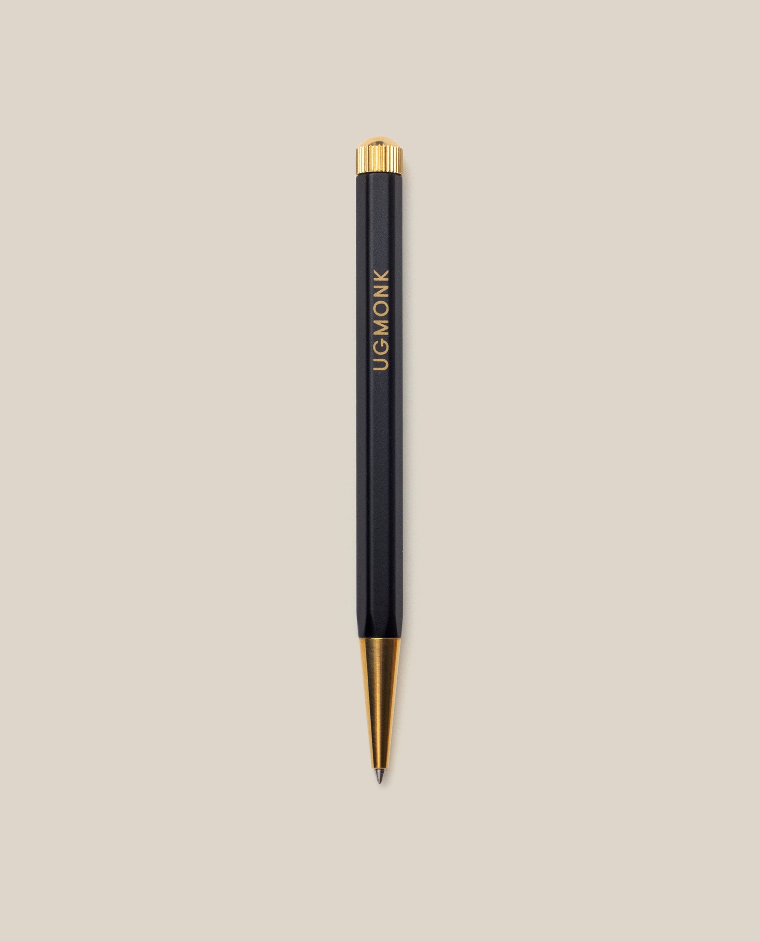 The Ugmonk Pen (Leuchtturm1917 Drehgriffel - Black) features gold accents and "UGMONK" printed vertically on its barrel, shown against a light beige background.