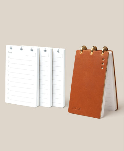 The Leather Discbound Analog + 3 Refills (Tan) with full-grain leather covers and three brass rings sits beside white lined Analog Task Cards with checkboxes, all arranged on a beige background.