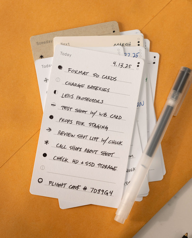 Analog - Task Cards (12-Pack) are used here as a handwritten photoshoot checklist—formatting SD cards, charging batteries, prepping props—with a pen and additional productivity cards on a tan surface.