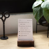 Analog - Today Cards (3-Pack), featuring a dot grid and to-do list tasks like "Email Sara" and "Order prototypes," rest on a wooden stand atop a desk with scissors, a plant, and part of a tan desk pad also in view.