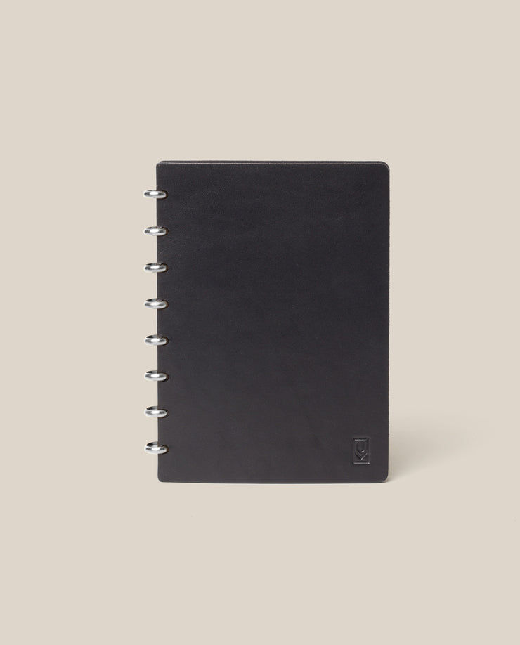 The Discbound Heirloom Journal (Black Leather - Standard 6" x 8.5") features a refillable design with a full-grain black leather cover and metal rings on the left, shown standing upright against a light beige background.