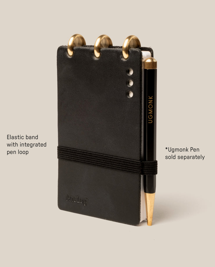The Leather Discbound Analog (Black) is made from full-grain black leather, features three gold discs at the top, an elastic pen loop with a black and gold Ugmonk pen (sold separately), supports Analog Task Cards, and has four silver rivets on the right.