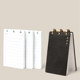 The Leather Discbound Analog + 3 Refills (Black), a compact black full-grain leather notepad with gold rings, stands upright beside three stacks of loose lined refill cards on a light beige background.