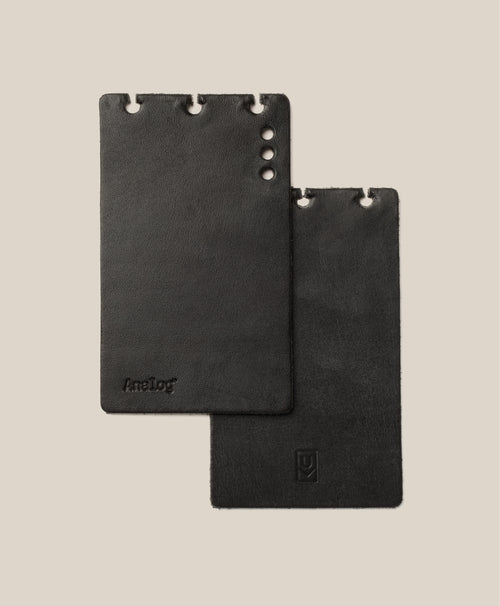 *Covers Only* – Leather Discbound Analog (Black) features two black full-grain leather covers with rounded corners and three holes along the top edge designed for Discbound Analog systems. Each cover displays a subtle embossed logo, and all are made in the USA. The background is a light beige color.