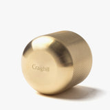 The Craighill Match Striker (Brass) is a gold-colored, cylindrical brass piece with a fine grip and rounded end. "Craighill" is engraved on its side. Designed for strike-anywhere matches, it’s pictured resting on its side against a white background.