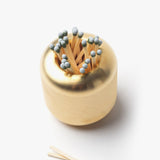 The Craighill Match Striker (Brass) is a gold, round solid brass holder filled with wooden matches, with three strike anywhere matches placed beside it on a white surface.