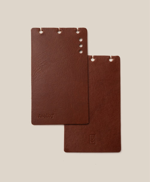 Two brown rectangular *Covers Only* – Leather Discbound Analog (Brown) made from full-grain leather, each with holes along the top edge, are placed on a beige background. One cover is embossed with “Analog,” while the other displays a small logo at the bottom. These Discbound covers are crafted in the USA, reflecting quality craftsmanship and timeless style.