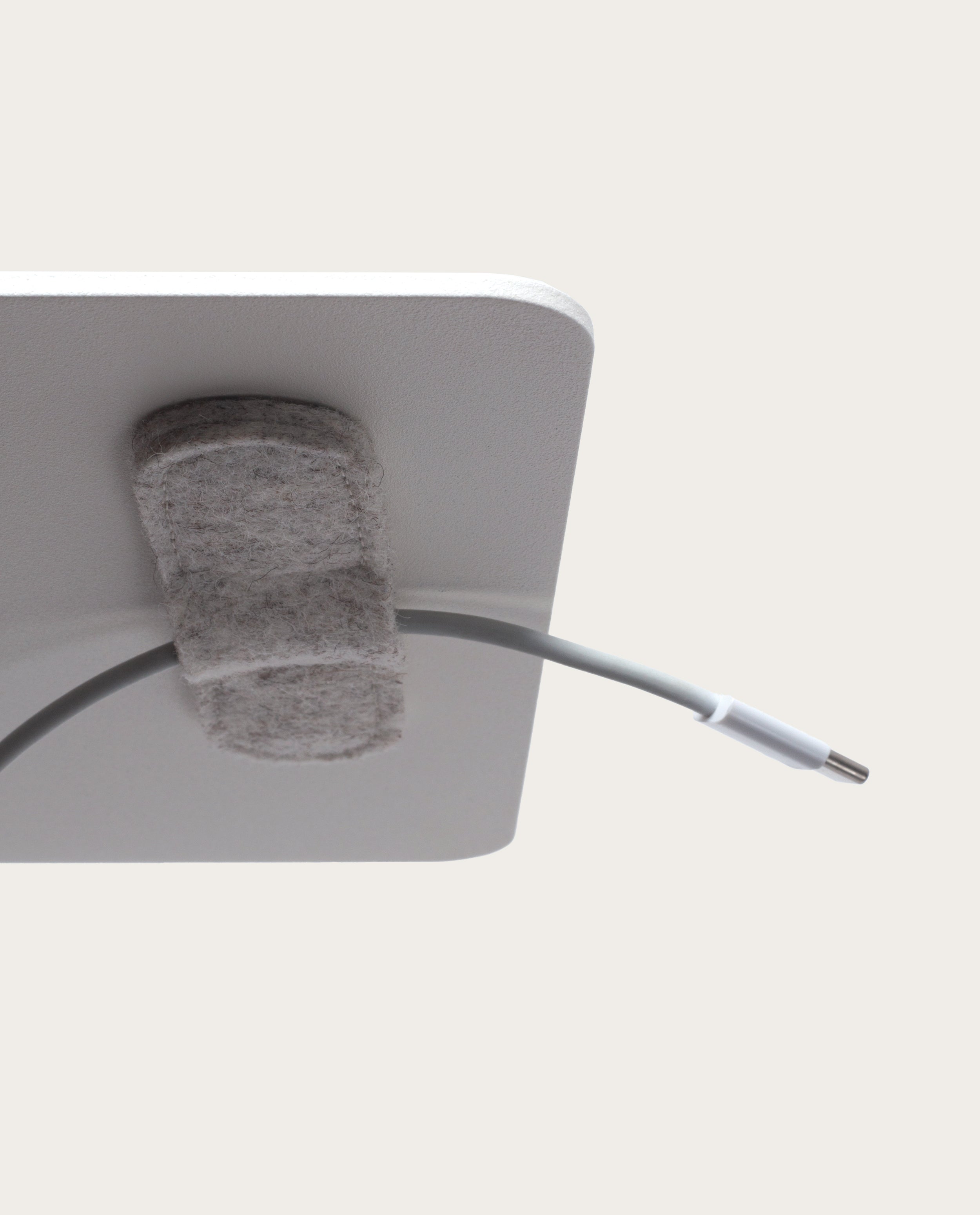 A close-up of the Warehouse Item - Magnetic Cable Keepers (Set of 2 - Light Gray), one of the most practical solutions for organizing cables, attached to the corner of a white surface and holding a white USB-C cable—an essential addition to your collection of monitor stand accessories.