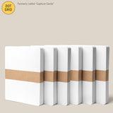 Six Analog Dot Grid Cards - Large (6-Pack) with white covers and a brown paper band are arranged in a row on a beige background. Previously called Capture Cards, they’re made from premium card stock and measure 5 x 6.5 inches.