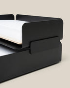 A close-up of the Capture Bundle—black steel small and large stackable trays—each tier holding white paper, shown against a beige background.