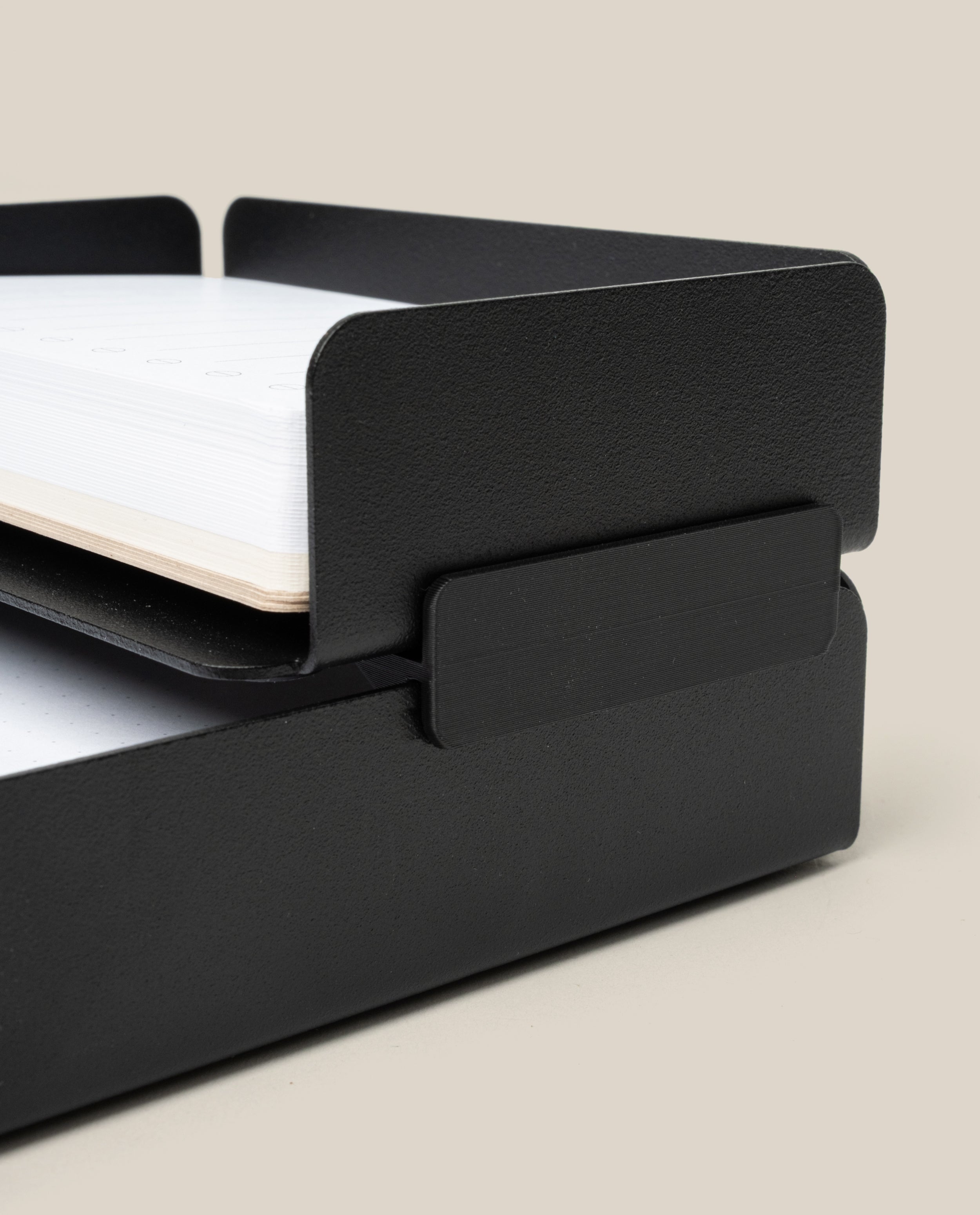 A close-up of the Capture Bundle—black steel small and large stackable trays—each tier holding white paper, shown against a beige background.