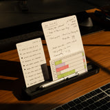 Sunlight illuminates handwritten notes with a to-do list and diagram, propped in the Analog Card Bar (Small 10" - Black) solid aluminum card holder, alongside a silver pen and part of a laptop keyboard.