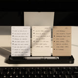 Three notecards with handwritten task lists are propped on the Analog Card Bar (Small 10" - Black), paired with a silver pen, all set behind a black keyboard on a warmly lit desk.