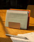 A metal pen holder displays colored index cards in Analog Card Sleeves - Large (Bright) on a wooden table, with a silver pen and a sheet of paper featuring sketches and handwritten notes nearby, all in warm sunlight.