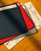 Four colored folders (navy, red, gray) are stacked on top of each other, partially covering handwritten notes and sketches on white paper, alongside Analog Card Sleeves - Large (Bright) arranged neatly on a wooden surface.