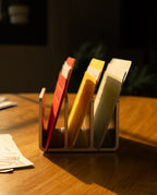 A set of Analog Card Sleeves - Small (Bright) in red, yellow, and beige are neatly arranged in a metal file and card organizer on a wooden table, with sunlight casting shadows across the scene.