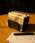 A black and brown desk organizer holds several file folders and a card organizer fitted with sleek Analog Card Sleeves - Small (Earth) on a wooden table. In front, a notepad with handwritten notes and a pen are placed. Warm light highlights the scene.