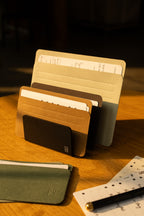 A desktop organizer holds neatly arranged file folders and papers on a wooden table, with sunlight casting warm shadows. Beside it, a card organizer fitted with Analog Card Sleeves - Large (Earth) keeps important cards tidy and accessible. A pen and planner page are placed nearby, suggesting a workspace setting.