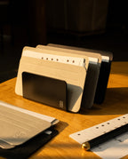 A set of neutral-colored index cards in Analog Card Sleeves - Small (Monochrome) is organized in a black card organizer on a wooden table, with additional cards and a pen beside it, all illuminated by warm sunlight.