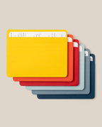 Seven colorful index cards—yellow, red, orange, dark gray, light gray, blue, and navy—are stacked askew with the yellow card on top partially revealing handwritten notes beneath. They fit neatly into the Analog Card Sleeves - Large (Bright), a practical organizer that keeps your notes secure and easily accessible.