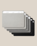 Six Analog Card Sleeves - Large (Monochromatic) in gradient shades from gray to black, each serving as a stylish organizer for stacks of handwritten white cards, are arranged in a slightly fanned, overlapping layout on a beige background.