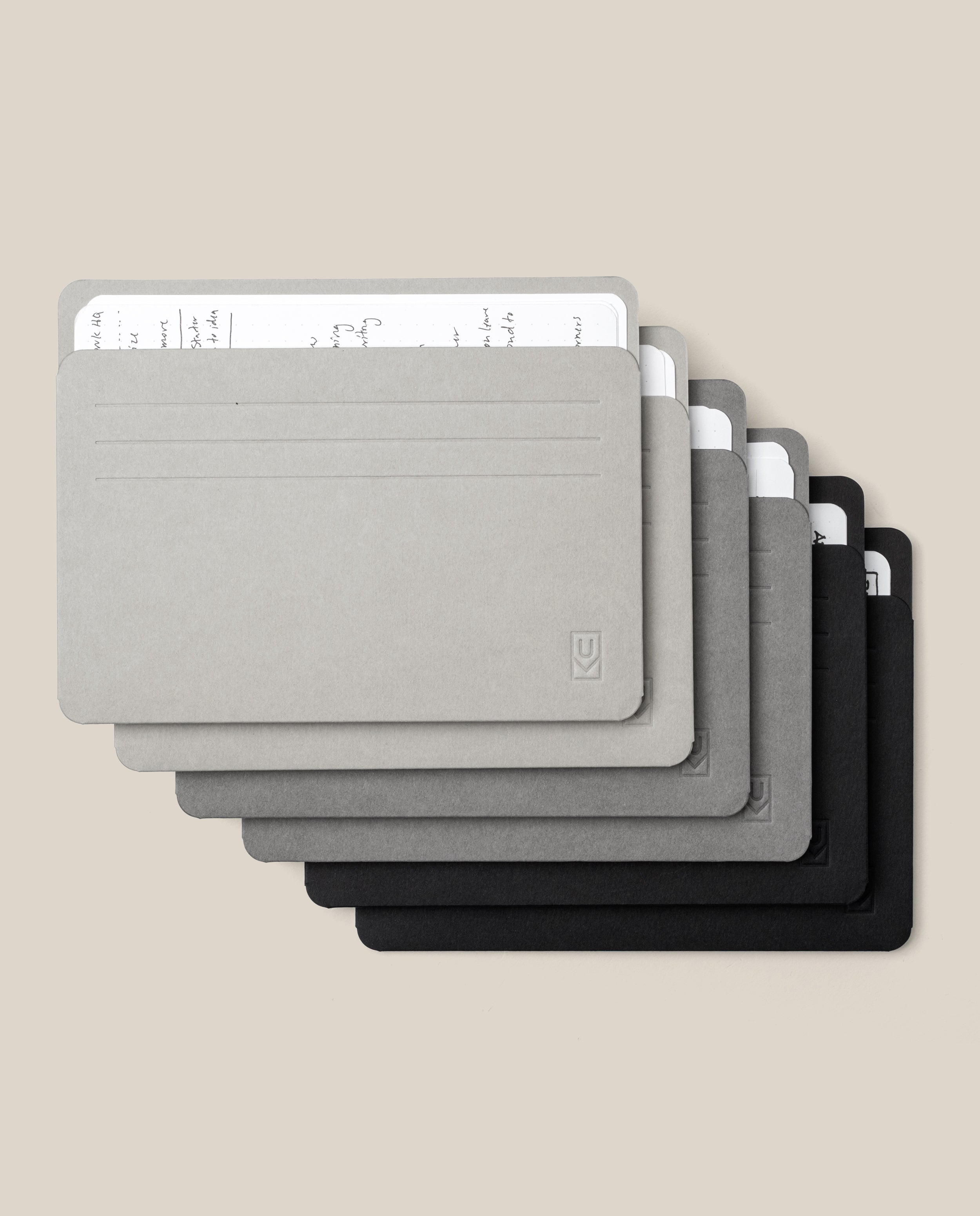 Six Large Analog Card Sleeves (Set of 6 – Monochromatic) in minimalist rectangular shapes and shades of grey and black are stacked in a fan arrangement, each organizer displaying handwritten notes peeking from the top.