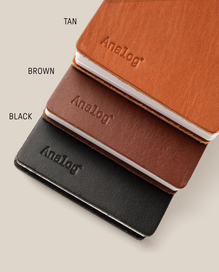 Three Leather Discbound Analog notebooks in tan, brown, and black with full-grain leather covers are stacked diagonally on a beige background. Each has "Analog" embossed on the cover with color labels beside each notebook.
