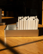 An Analog Archive (Silver Aluminum) desk card file filled with index cards, sitting on a wooden desk.