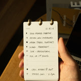 A hand holds the Discbound Analog + 3 Refills planner, open to a to-do list dated 12.16.24 with tasks like sending creative updates, reviewing a moodboard, ordering swatches, scheduling a photoshoot, brainstorming, and making calls.