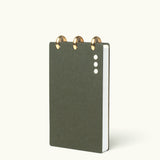 A compact, dark green Discbound Analog + 3 Refills notebook with brass disc binding and three white cover dots, shown upright against a light background—stylish and refillable for organizing tasks.