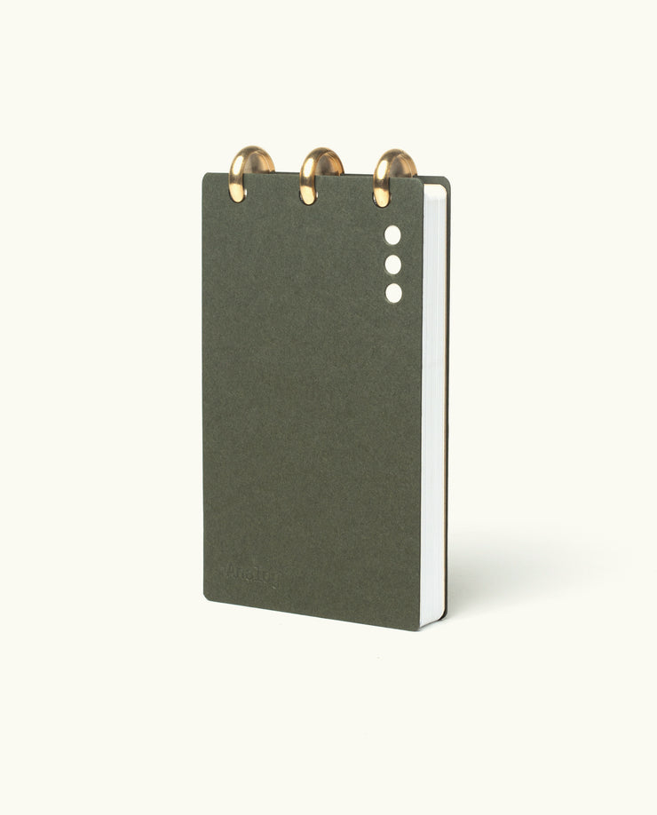 A compact, dark green Discbound Analog + 3 Refills notebook with brass disc binding and three white cover dots, shown upright against a light background—stylish and refillable for organizing tasks.